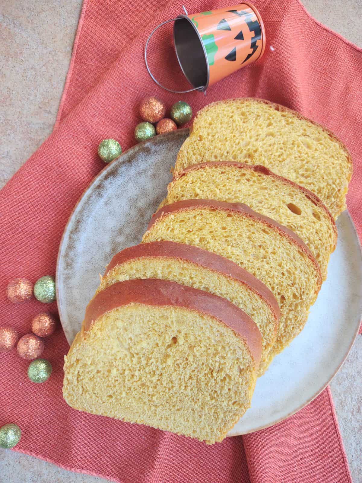 Slices of pumpkin yeast bread on a gray and brown plate on top of an orange towel.