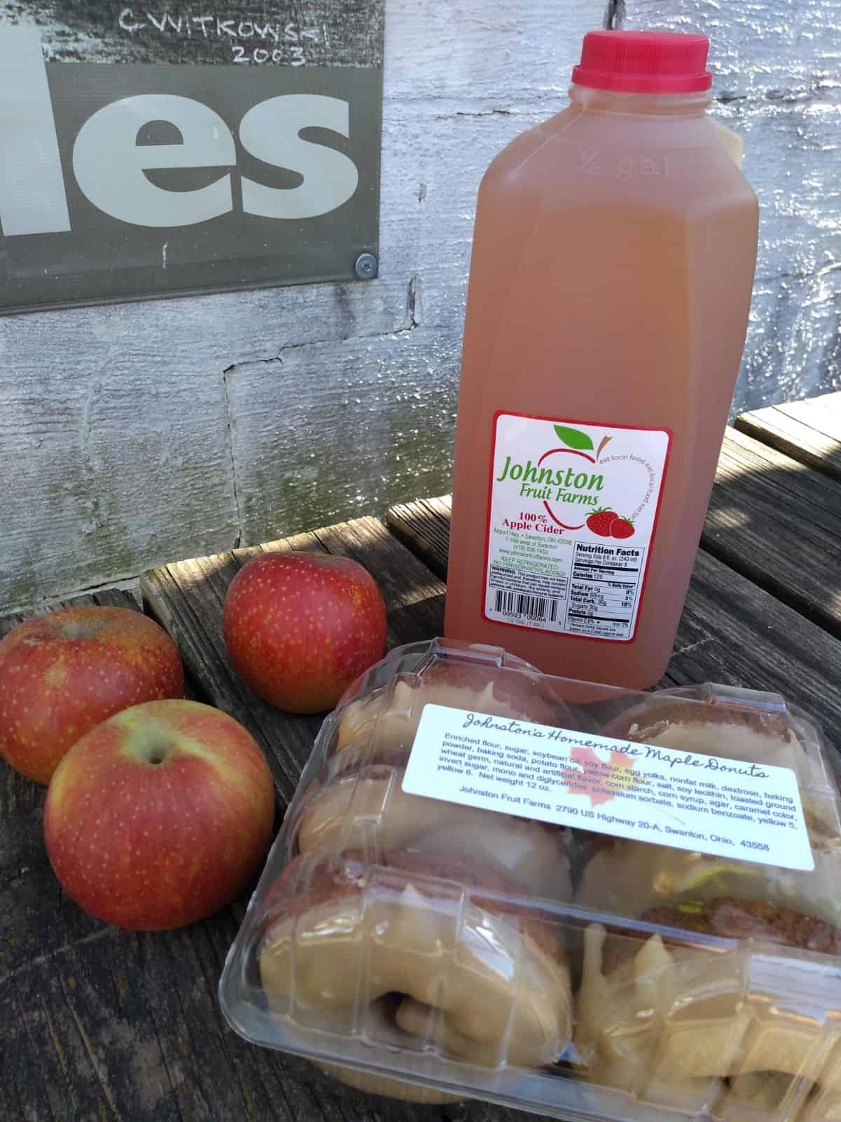 Johnston Fruit Farms apple cider, maple donuts, and apples on a picnic table.