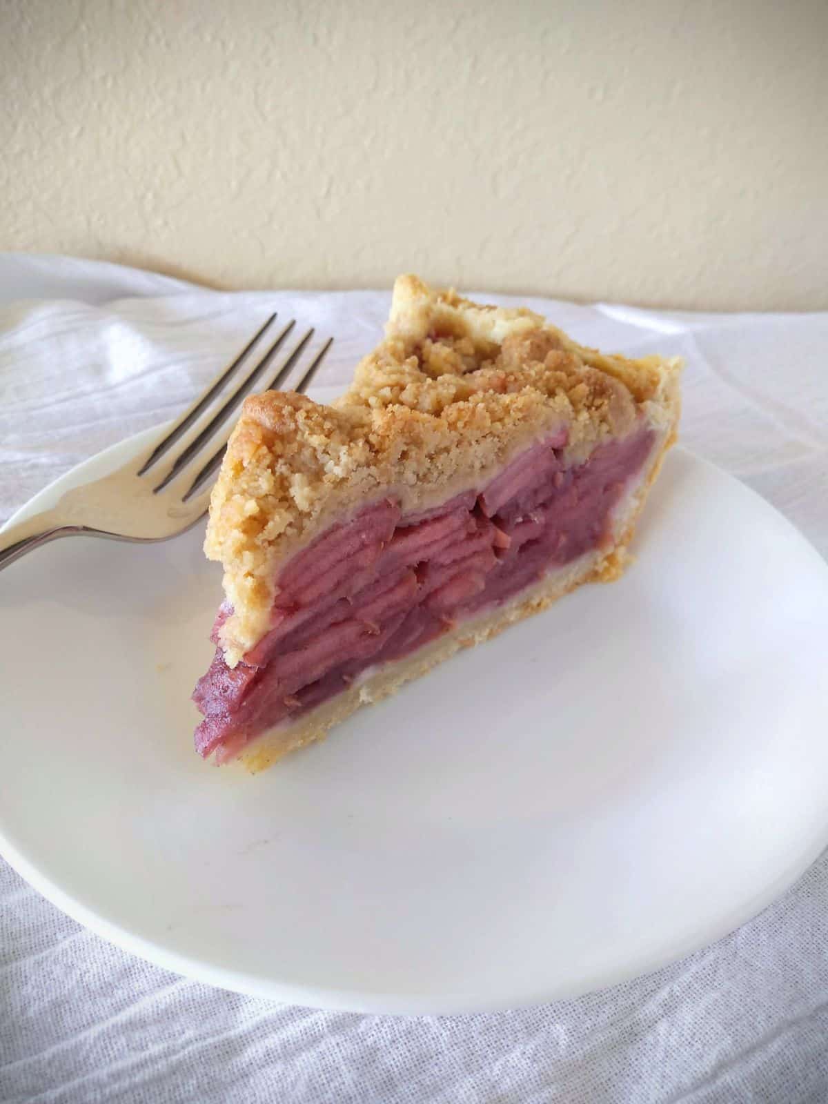 A slice of apple pie on a plate. The apples are red in color.