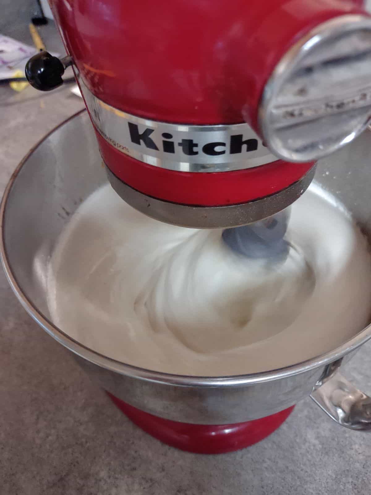 Red KitchenAid Stand Mixer with marshmallows being whipped inside the bowl.