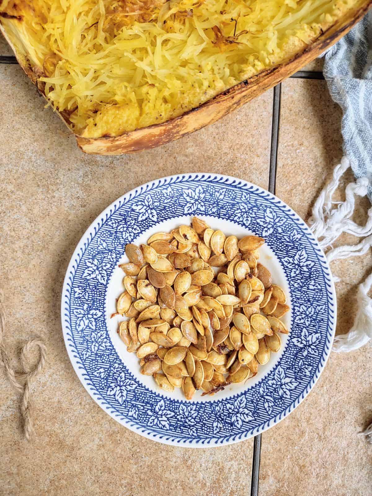 A plate of roasted spaghetti squash seeds next to a cooked spaghetti squash.