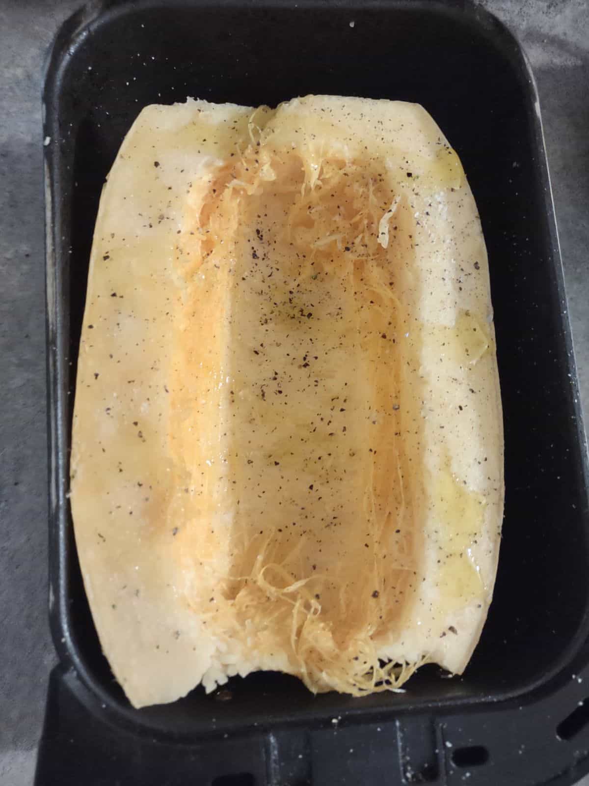 A half of a spaghetti squash with the ends trimmed inside of an air fryer basket.