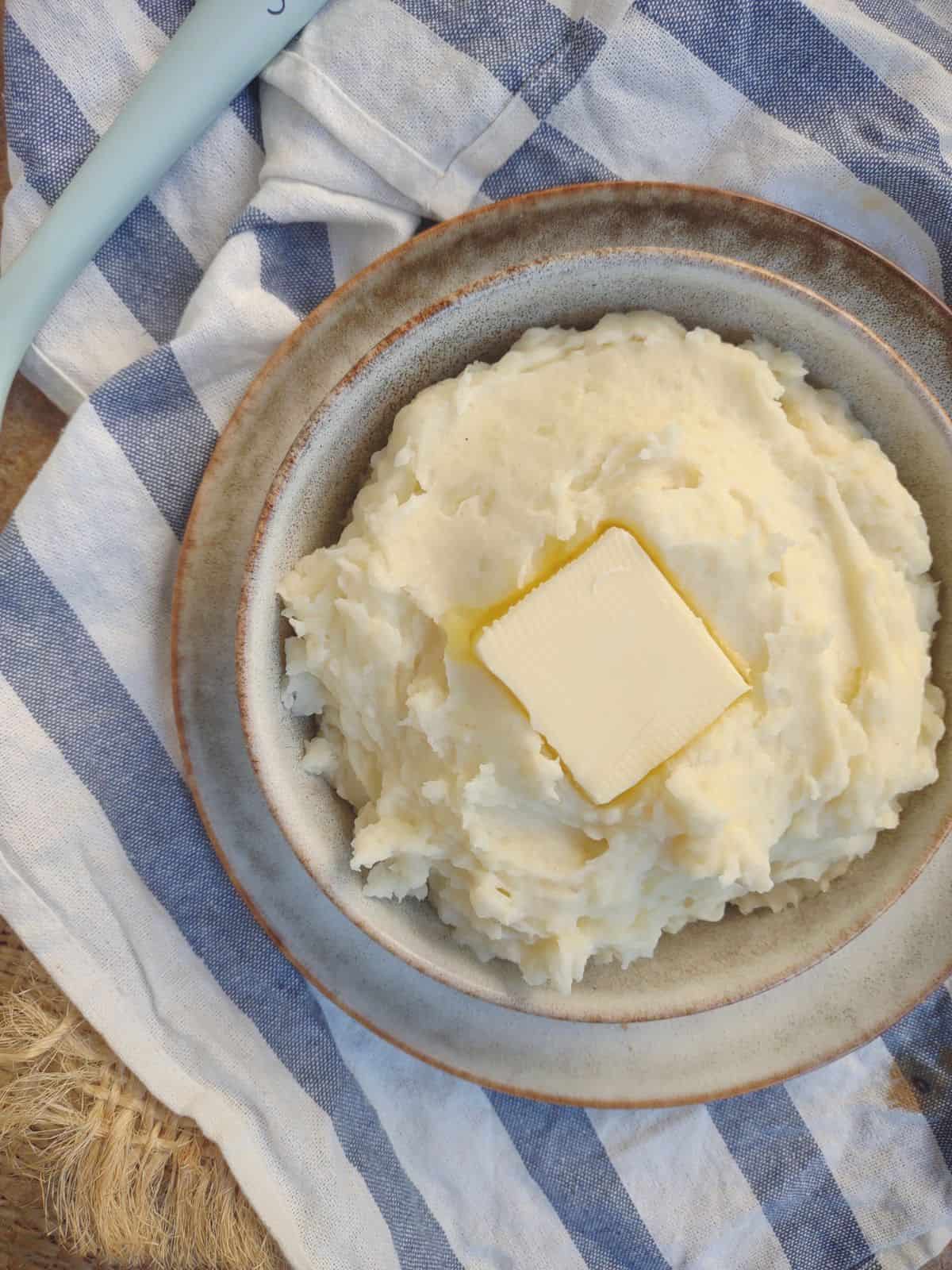 A bowl of mashed potatoes with a big pat of butter in the center. 