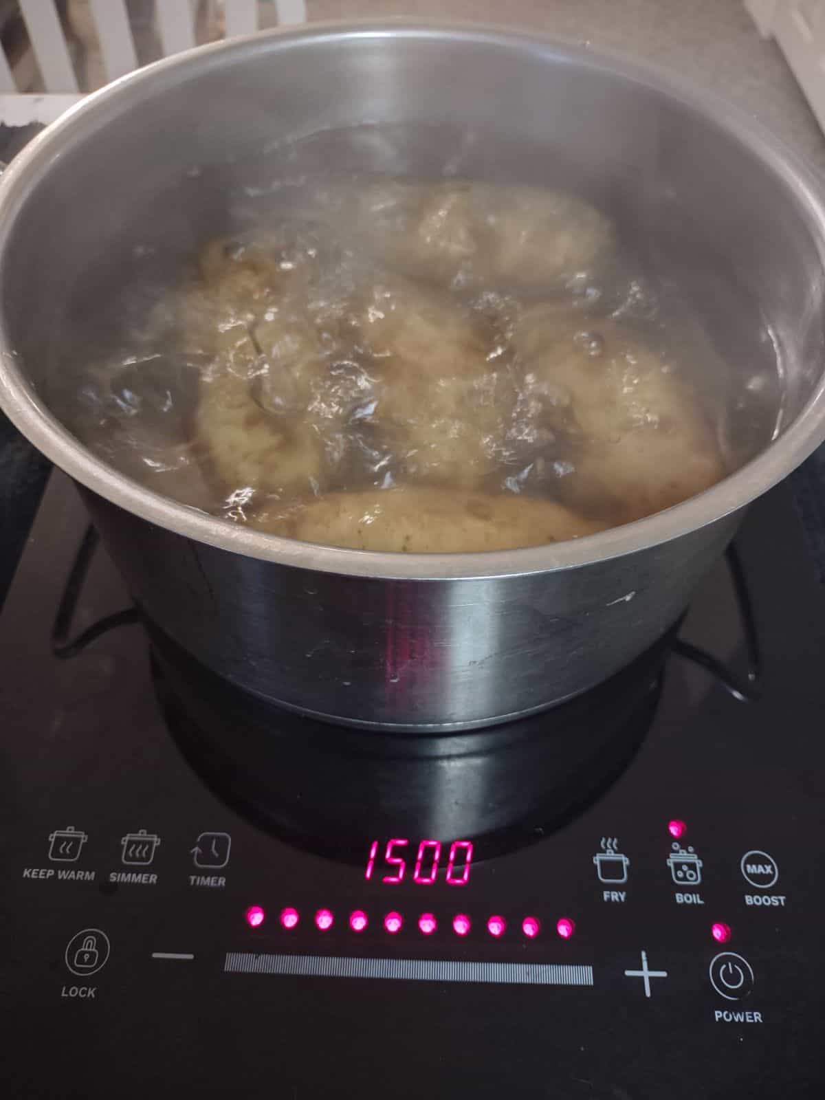 Russet potatoes boiling in a large wide pot. 