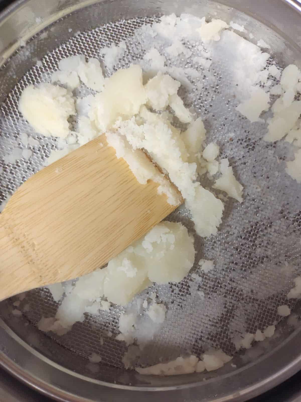A wooden spatula is pushing cooked potatoes through a sieve.