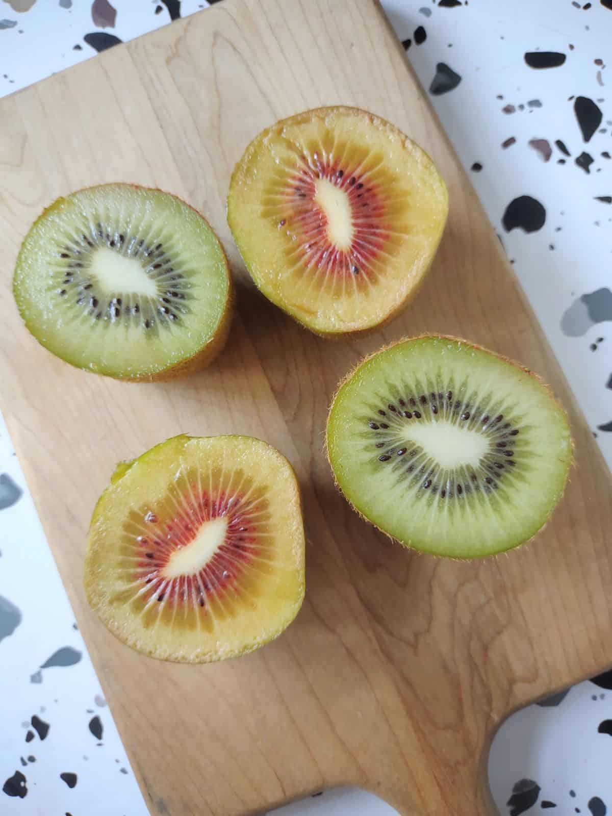 Kiwi cut in half, one is green on the inside and he other is yellow with a red ring in the middle.