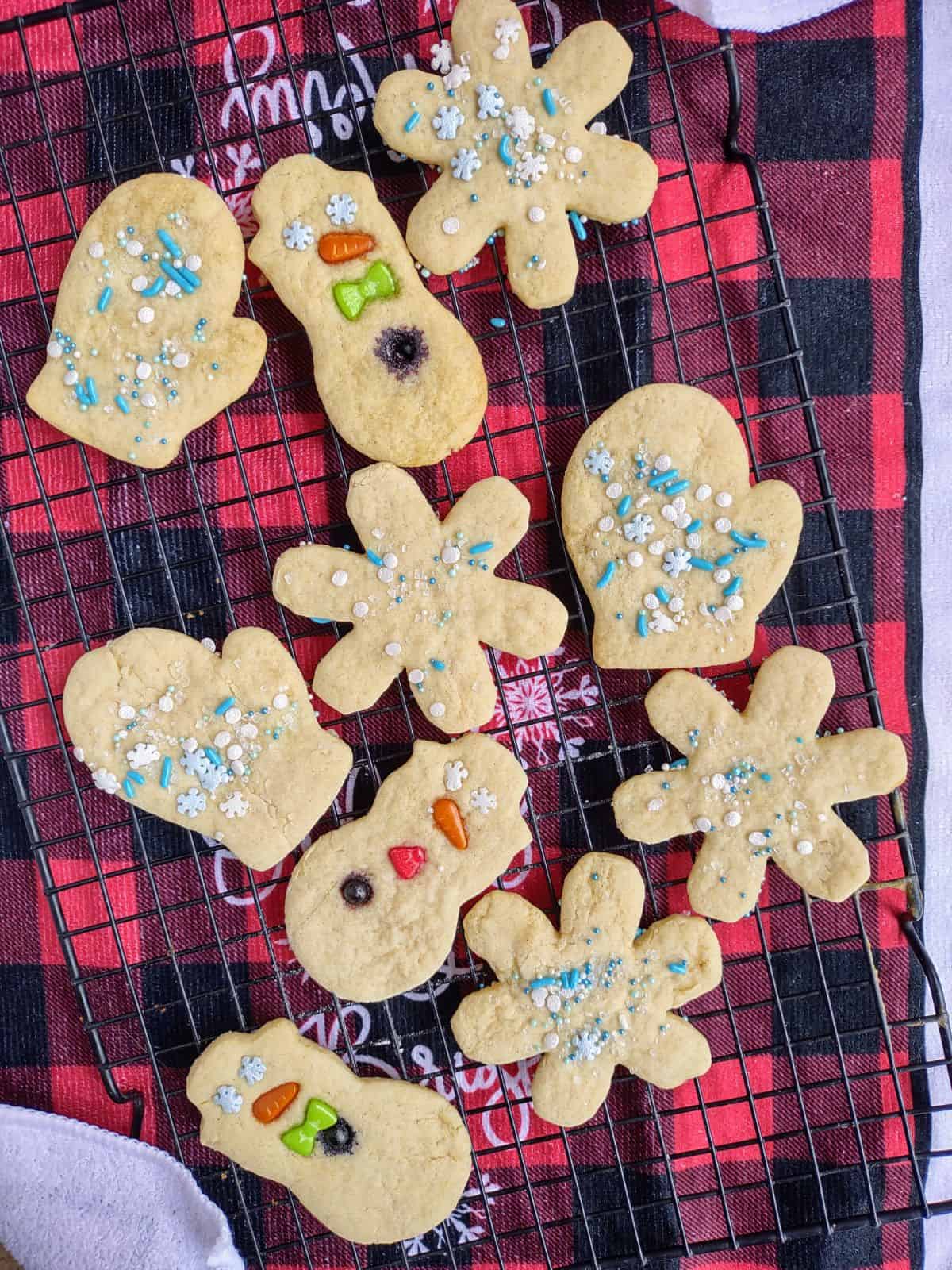 Decorated sugar cookies without frosting on a dry rack with a red plaid towel underneath.