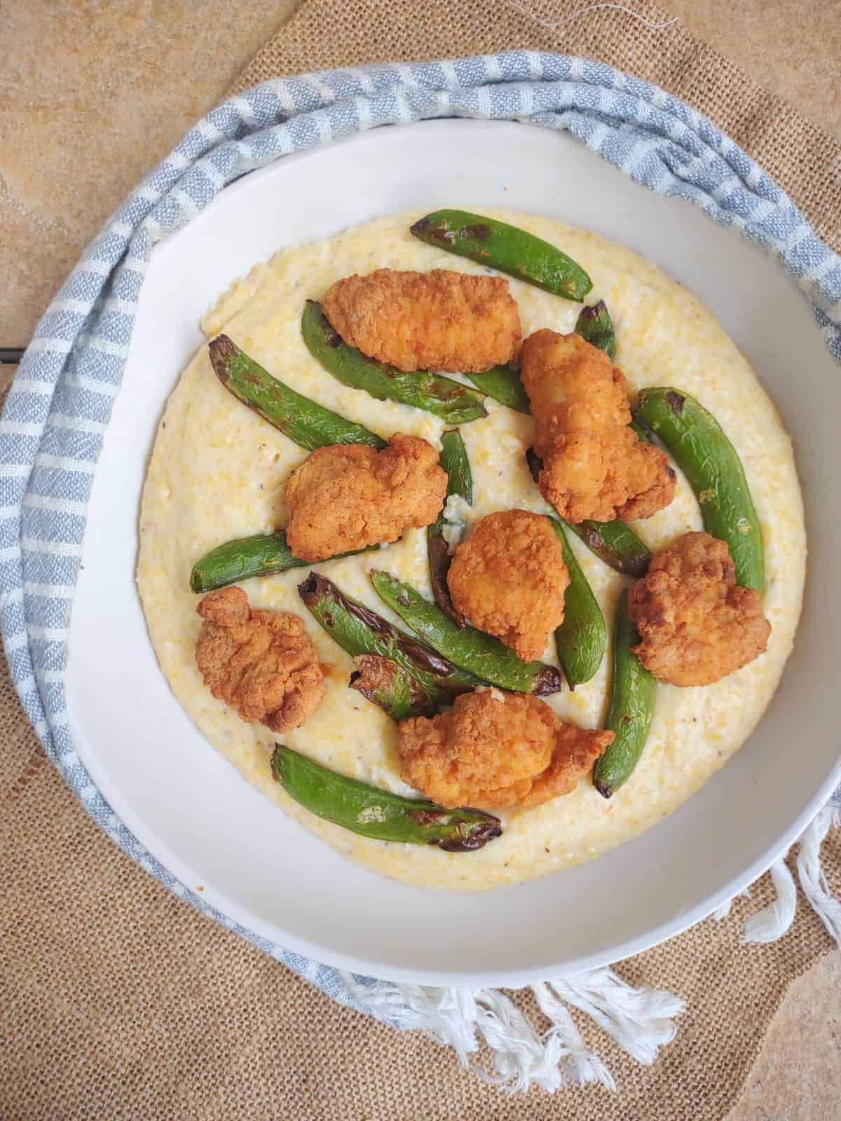 Yellow corn grits in a bowl topped with Kirkland Lightly Breaded Chicken Breast Chunks and air fried snap peas.