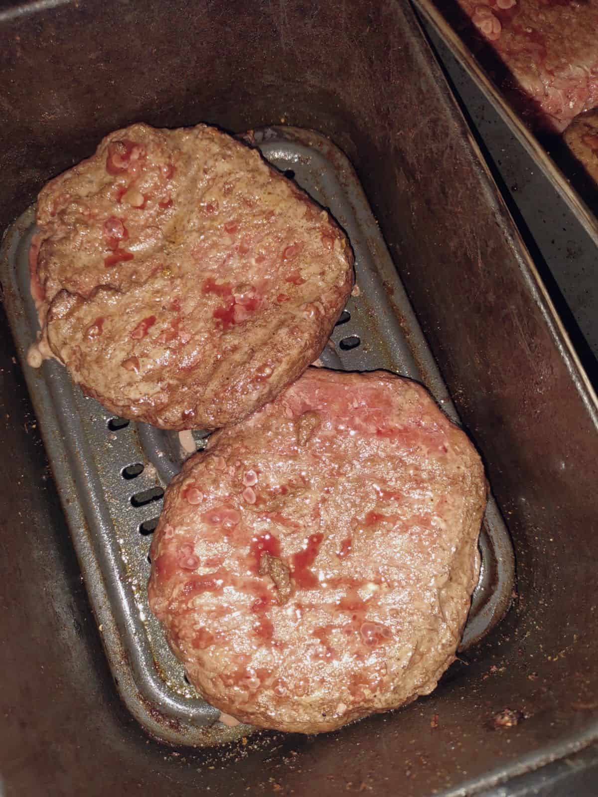Partly cooked burger patties in an air fryer basket.