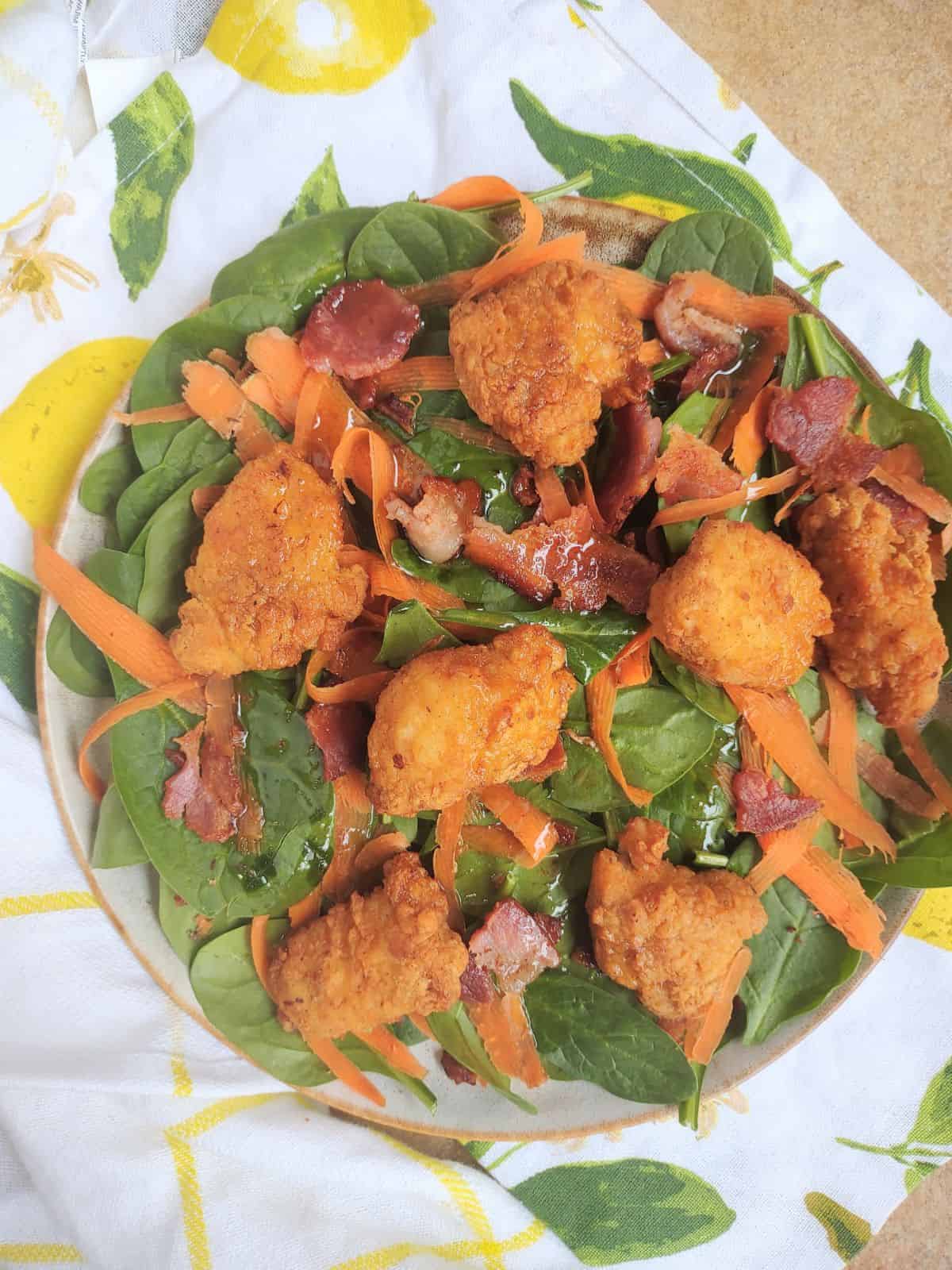 A spinach salad topped with Kirkland Lightly Breaded Chicken Breast Chunks, carrots, and bacon with a warm bacon dressing.