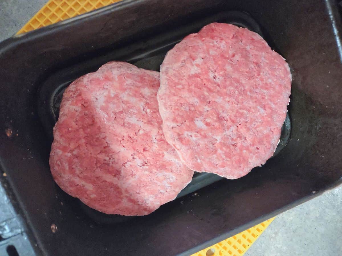 Raw burger patties in an air fryer basket.