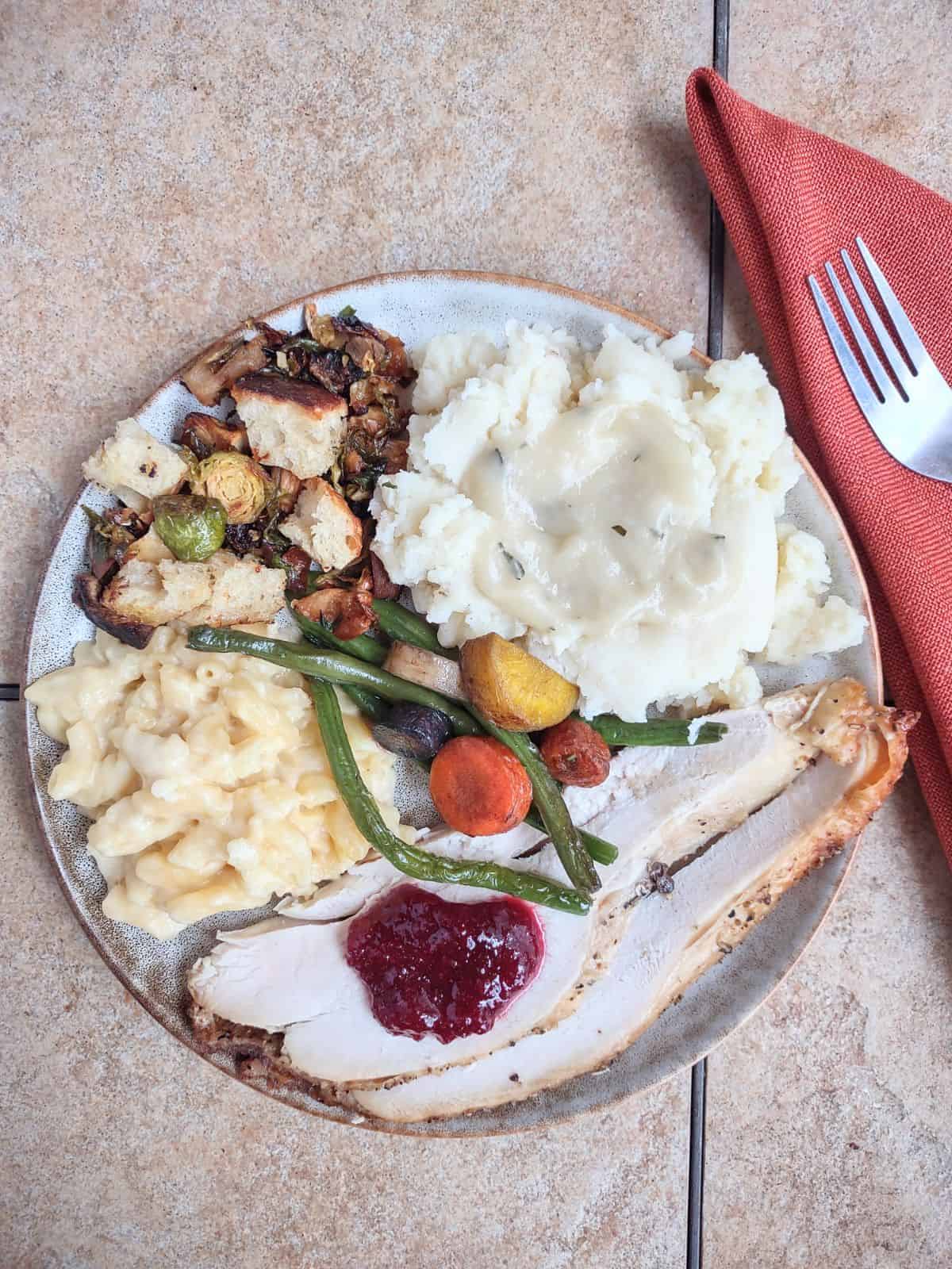A plate of Thanksgiving food (turkey, mashed potatoes, carrots, green beans, dressing, and cranberry sauce).
