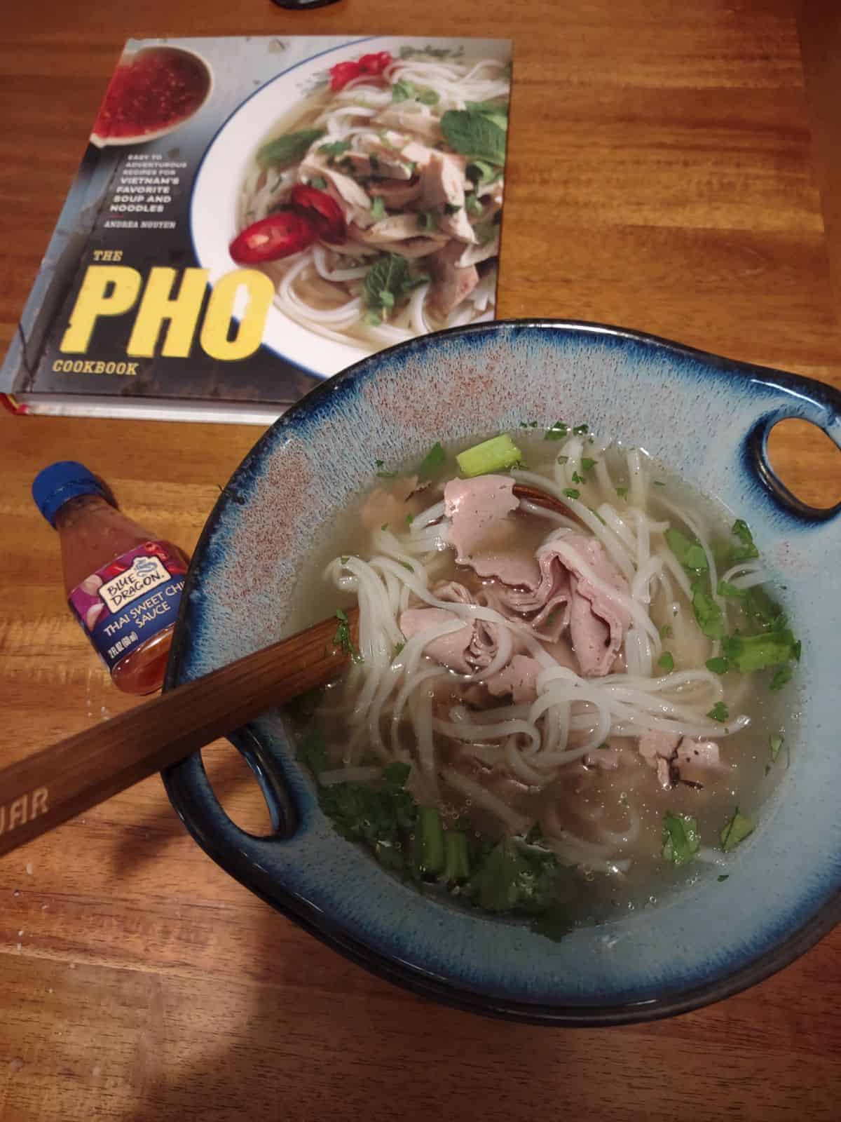 A bowl of roast beef pho sitting next to the Pho cookbook.