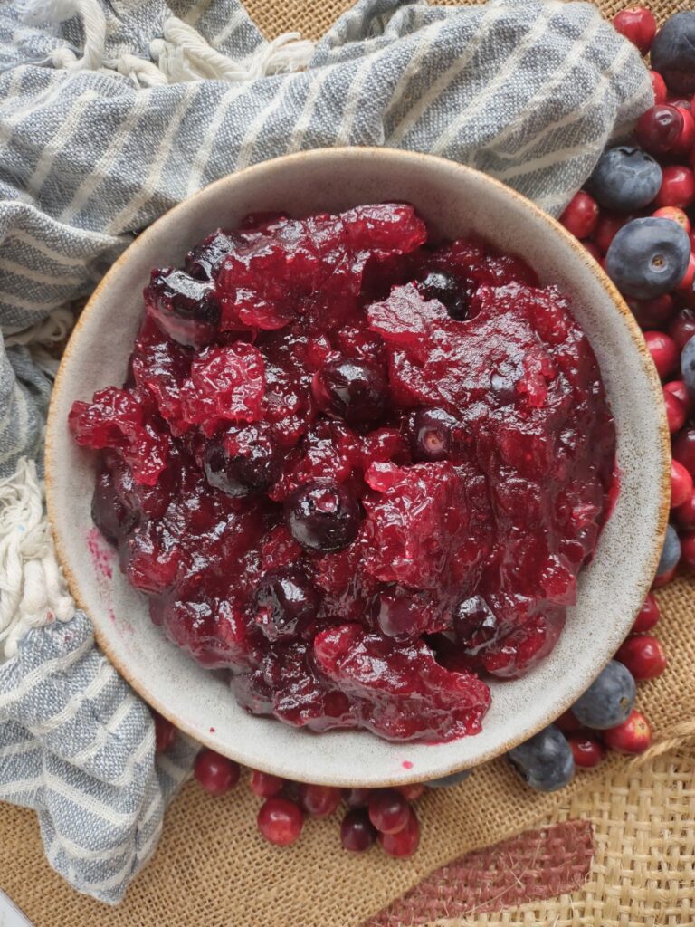 A bowl filled with cranberry sauce that contains fresh blueberries and cardamom