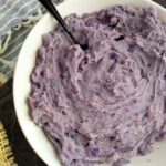 A white bowl filling with purple mashed potatoes with a black spoon sticking out.
