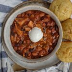 A bowl filled with chili with black beans, pinto beans, smoked turkey, hatch chilies, sautéed onions, and a dollop of sour cream on top.