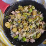 Sautéed Brussels Sprouts halves in a cast iron pan with chunks of leftover smoked turkey topped with Parmesan cheese