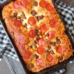 A Detroit style pizza in a cast iron casserole on top of black and white towels.