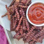 Crinkle cut purple sweet potato fries on a sheet pan with ketchup