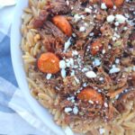 A close up of a bowl filled with a Greek Inspired Beef Pot Roast with carrots and feta on top of a bed of toasted orzo pasta