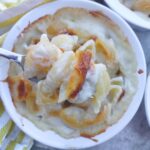 A fork holding up white cheddar shell mac and cheese over top of a ramekin with baked mac and cheese.