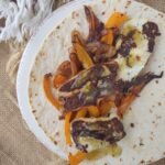 Panela cheese tacos with onions, orange bell peppers, and green taco sauce on a soft taco flour tortilla