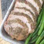 A pork sirloin roast that has been sliced diagonally on a sheet pan with green beans.