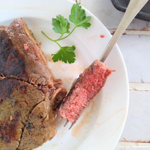 A bite of Ranch being held up with a fork over the cooked steak
