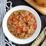 Beef and barley soup with carrots and dill in a white bowl.