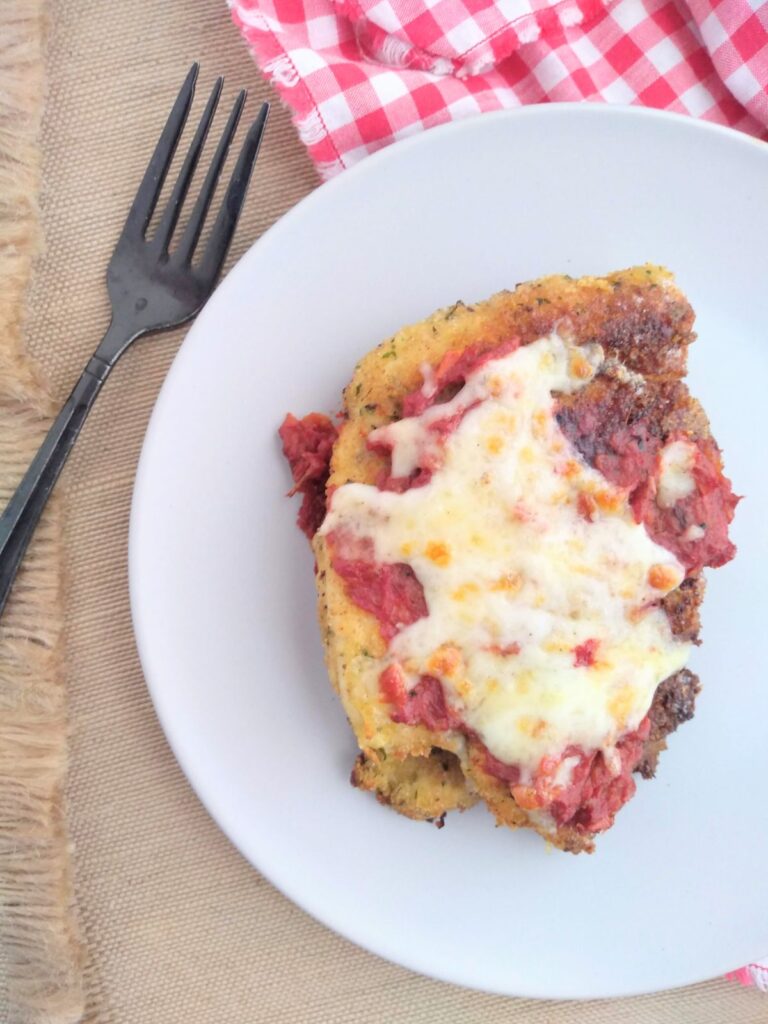 A single piece of Chicken Parmesan on a white plate with a black fork next to the plate.