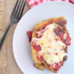 A single piece of Chicken Parmesan on a white plate with a black fork next to the plate.