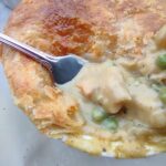 A fork showing the interior of an a puff pastry pot pie in a ramekin.