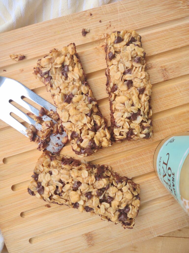 3 Tahini Chocolate Chip Granola bars on a wood cutting board with a metal spatula and a bottle of Tahini.