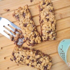 3 Tahini Chocolate Chip Granola bars on a wood cutting board with a metal spatula and a bottle of Tahini.