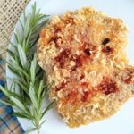 Pork chops that are breaded with crushed Ramen noodles and breadcrumbs on a white plate in rosemary.