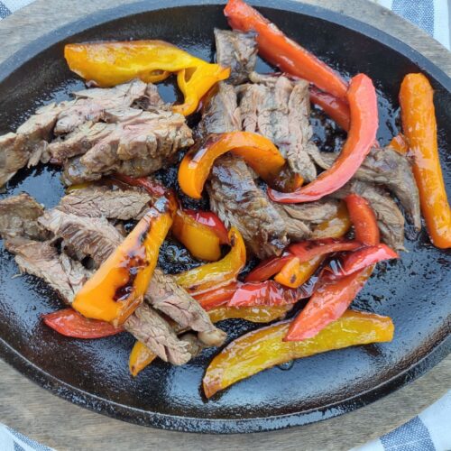 Skirt steak on a single serving cast iron skillet with red and orange bell peppers