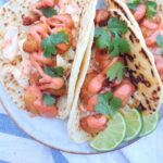3 Fried shrimp tacos with homemade slaw, sauce, lime on a plate.