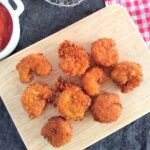 Panko Fried Shrimp on a small cutting board surrounding by different types of towels and a bowl of ketchup and a mesh spider.