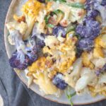 A plate of yellow, white, and purple cauliflower coated in a tahini sauce.