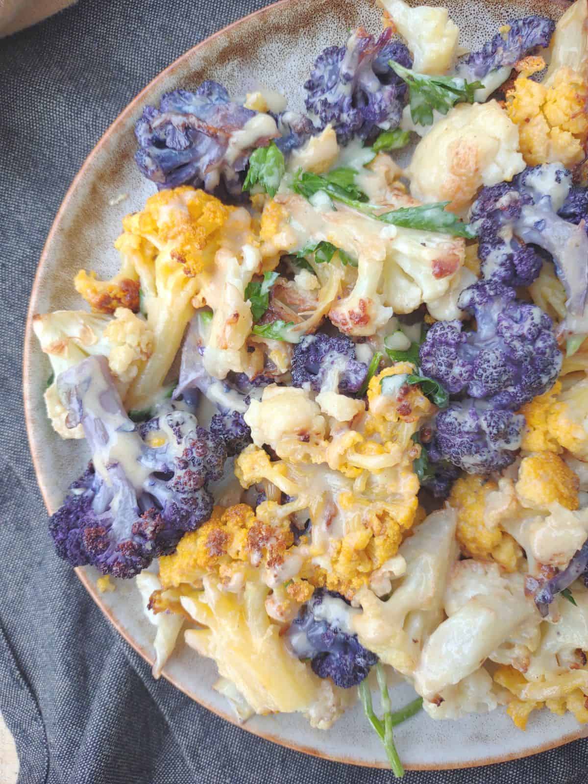 A plate of yellow, white, and purple cauliflower coated in a tahini sauce.