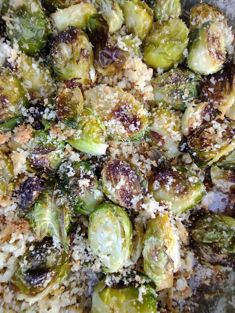 Up close view of roasted Brussels sprouts on a sheet pan with Panko breadcrumbs and Parmesan cheese.