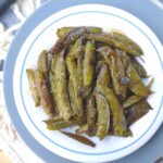 Roasted snap peas with honey on a white plate on top of a blue plate and white and blue stripe towel.