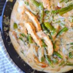 Chicken and asparagus in a cream sauce in a cast iron skillet.