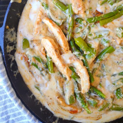 Chicken and asparagus in a cream sauce in a cast iron skillet.