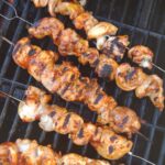 Grilled marked Chicken thigh skewers on the grill with BBQ sauce brushed on on the chicken.