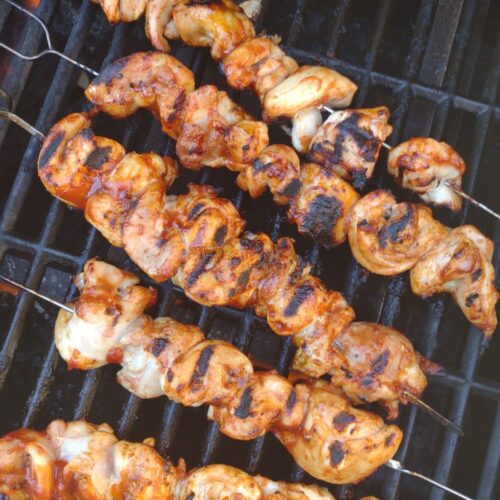 Grilled marked Chicken thigh skewers on the grill with BBQ sauce brushed on on the chicken.