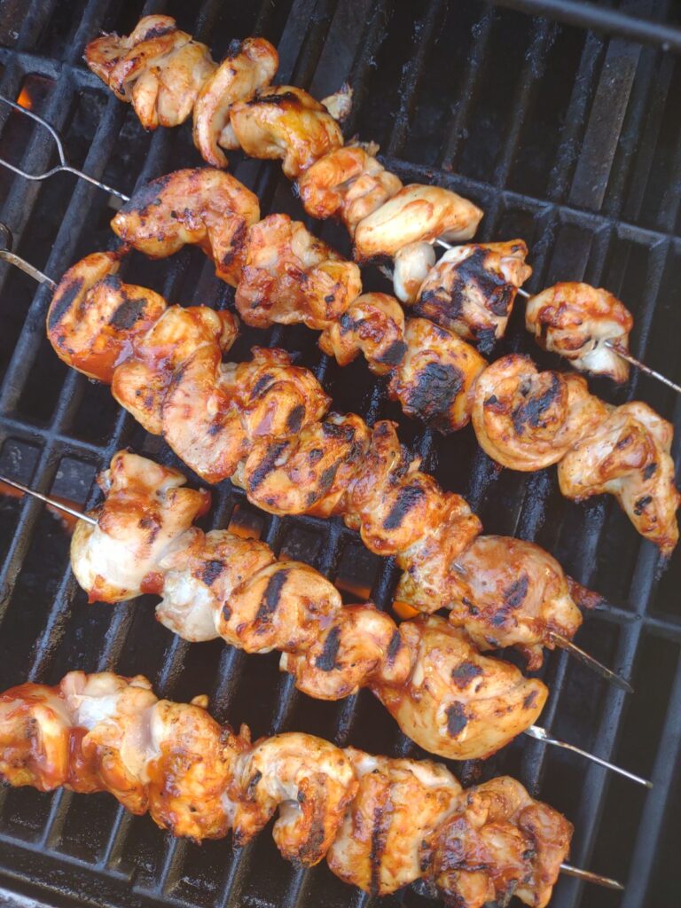 Grilled marked Chicken thigh skewers on the grill with BBQ sauce brushed on on the chicken.