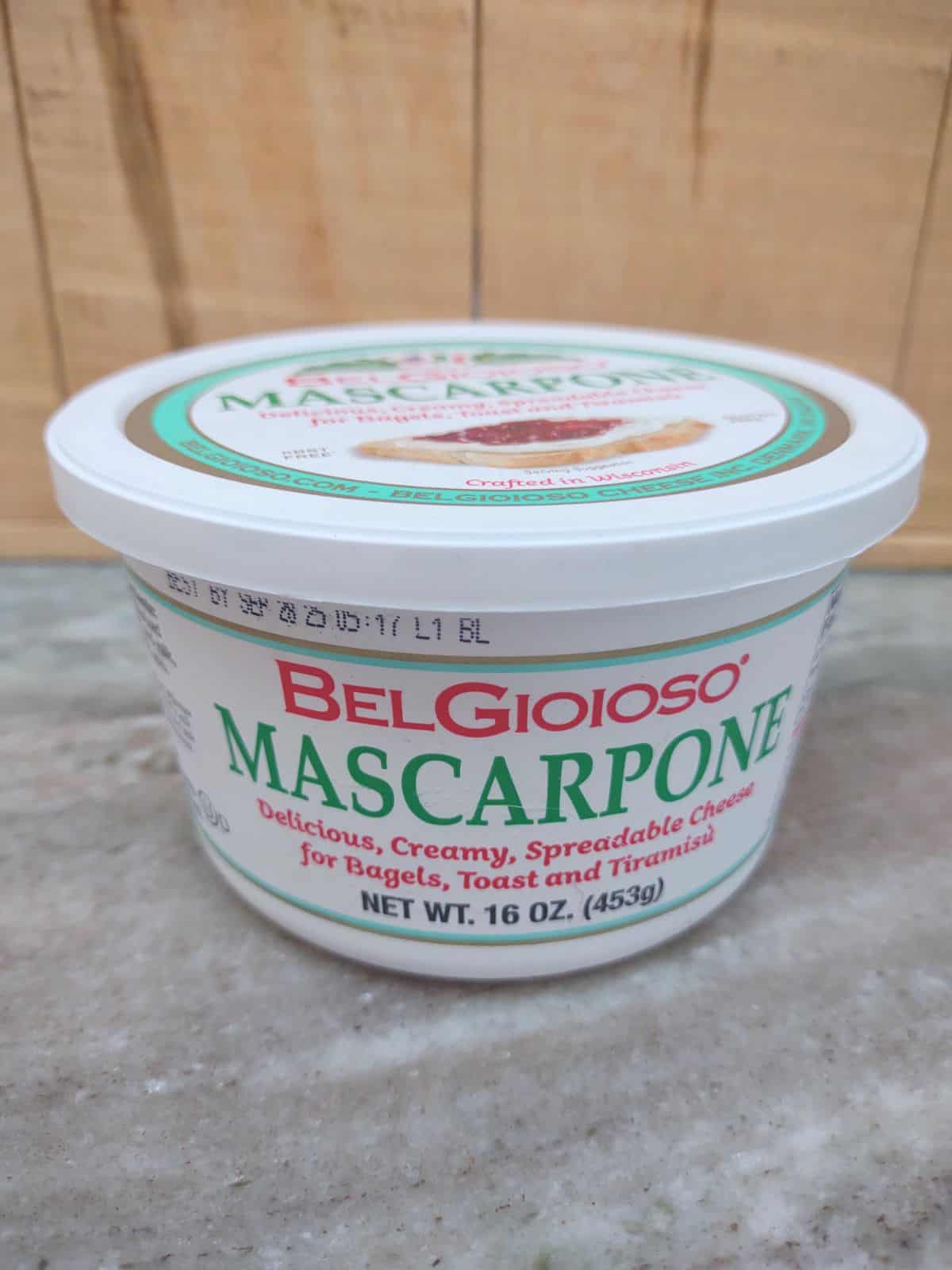 BelGioIoso Mascarpone cheese tub in front of a wood board.