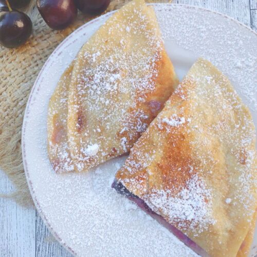 Two triangle slices of Cherry Dessert quesadilla filled Mascarpone on a white plate.
