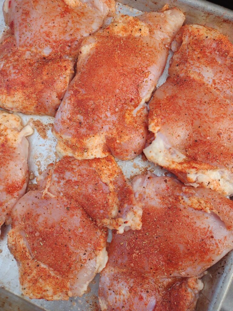 Raw chicken thighs with a dry rub on a sheet pan.